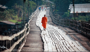 A monk crosses the Sangkhale River on the wooden bridge.